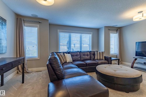 Carpeted living area with multiple windows, recessed ceiling speaker, and flush mount lighting fixtures - 233 Hawks Ridge Boulevard Nw, Edmonton, AB 