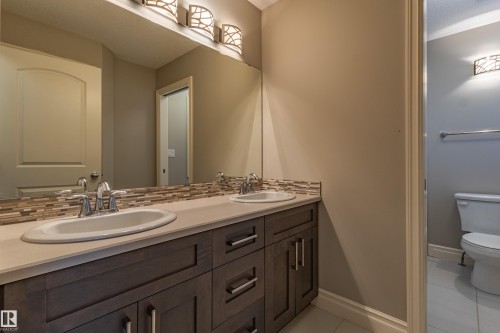Dual undermount sinks, wood-finish vanity with storage, stone-finish countertop, decorative tile backsplash, and overhead vanity lighting - 233 Hawks Ridge Boulevard Nw, Edmonton, AB 