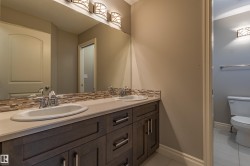 Dual undermount sinks, wood-finish vanity with storage, stone-finish countertop, decorative tile backsplash, and overhead vanity lighting - 