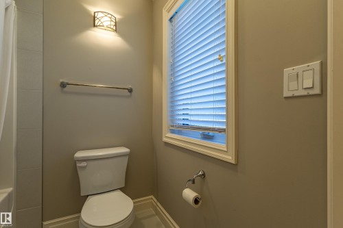 Bathroom featuring a window with blinds, a wall-mounted light fixture, a porcelain toilet, and a towel bar - 233 Hawks Ridge Boulevard Nw, Edmonton, AB 