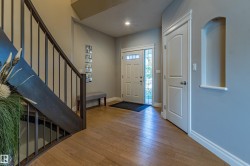 Wood-finish flooring, staircase with dark wood railing, white paneled doors, and recessed wall niche - 
