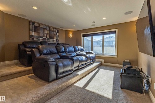Carpeted tiered seating area with recessed lighting, integrated ceiling speakers, and a large window with privacy blinds - 233 Hawks Ridge Boulevard Nw, Edmonton, AB 