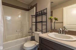 Tub and shower combination with chrome fixtures, vanity with integrated sink, and wood-finish cabinetry - 