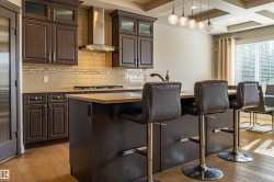Dark wood cabinetry with glass-front accents, stainless steel range hood, light wood-finish flooring, and a multi-pendant light fixture - 