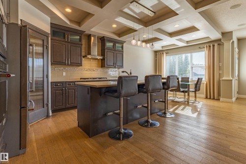 Kitchen featuring dark wood-finish cabinetry, stainless steel appliances, a central island with seating, and wood-finish flooring - 233 Hawks Ridge Boulevard Nw, Edmonton, AB 