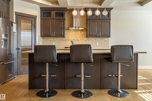 Kitchen featuring dark wood cabinetry with glass accents, stainless steel appliances, a range hood, and a decorative tile backsplash - 233 Hawks Ridge Boulevard Nw, Edmonton, AB 
