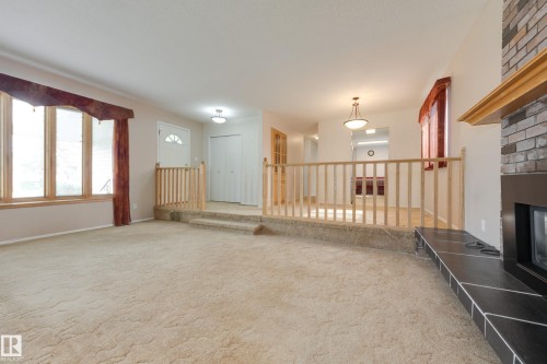 Bay window with wood trim, brick fireplace with wood mantel, carpeted flooring, and a two-step entry with wood railing - 3421 135A Avenue Nw, Edmonton, AB 