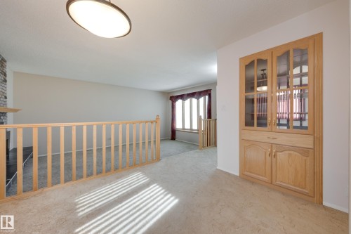 Built-in wood-finish cabinetry with glass panel doors, wood-finish railing, and a stone-clad fireplace - 3421 135A Avenue Nw, Edmonton, AB 