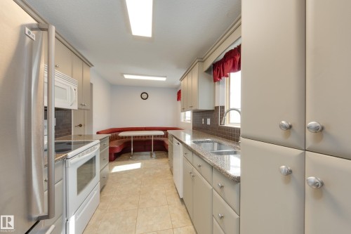 Kitchen featuring a built-in banquette, tile flooring, stone-finish countertops, stainless steel sink, and light-toned cabinetry - 3421 135A Avenue Nw, Edmonton, AB 