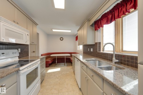Well-appointed kitchen featuring light-toned cabinetry, a double basin stainless steel sink, and granite-style countertops - 3421 135A Avenue Nw, Edmonton, AB 
