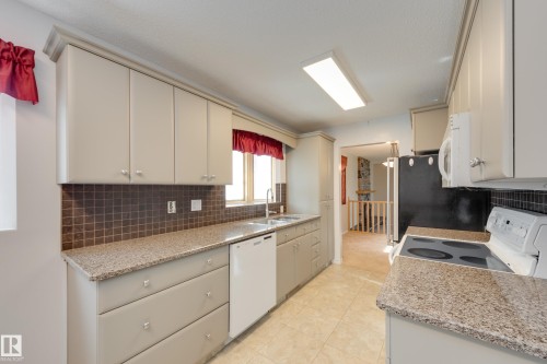 Kitchen featuring light-toned cabinetry, speckled countertops, and a tiled backsplash - 3421 135A Avenue Nw, Edmonton, AB 