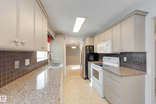 Kitchen featuring light-toned cabinetry, granite-finish countertops, square tile backsplash, and tile flooring - 3421 135A Avenue Nw, Edmonton, AB 