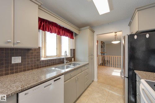 Kitchen featuring light-toned cabinetry, a double basin stainless steel sink, granite-style countertops, and a tiled backsplash - 3421 135A Avenue Nw, Edmonton, AB 