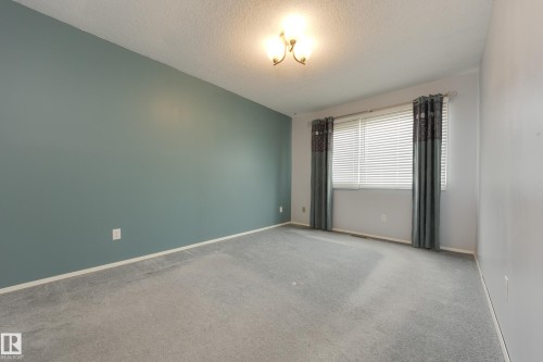 Carpeted flooring, window with blinds, wall-mounted light fixture, and a contrasting accent wall - 3421 135A Avenue Nw, Edmonton, AB 