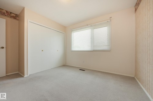 Light gray carpeting, a large window with horizontal blinds, and a bi-fold closet with brass-tone hardware - 3421 135A Avenue Nw, Edmonton, AB 