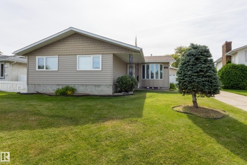 Front exterior featuring beige horizontal siding, gambrel-style roof with brown shingles, and a bay window - 3421 135A Avenue Nw, Edmonton, AB 