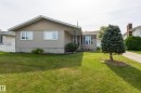 Front exterior featuring beige horizontal siding, gambrel-style roof with brown shingles, and a bay window - 3421 135A Avenue Nw, Edmonton, AB 