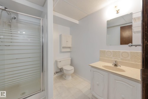 Glass-enclosed shower, white vanity with integrated sink, wall-mounted mirror, and tiled backsplash - 3421 135A Avenue Nw, Edmonton, AB 