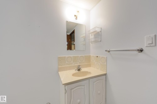 Vanity with an integrated sink, patterned tile backsplash, wall-mounted mirror, and overhead lighting - 3421 135A Avenue Nw, Edmonton, AB 
