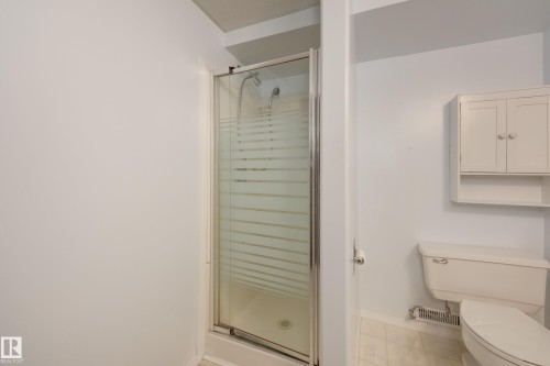 Shower enclosure with frosted glass, white wall-mounted cabinet with open shelving, and white toilet - 3421 135A Avenue Nw, Edmonton, AB 