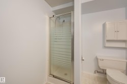 Shower enclosure with frosted glass, white wall-mounted cabinet with open shelving, and white toilet - 