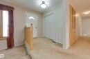 Entryway featuring a white paneled door with an arched window, light-toned wood-finish railing, and a built-in cabinetry with glass-front display - 3421 135A Avenue Nw, Edmonton, AB 