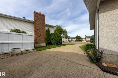 Concrete driveway leading to the property, featuring a brick chimney and white siding - 3421 135A Avenue Nw, Edmonton, AB 