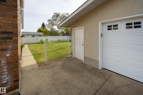 Attached garage with an overhead door featuring upper window panels, a side entry door, and a stucco exterior - 3421 135A Avenue Nw, Edmonton, AB 