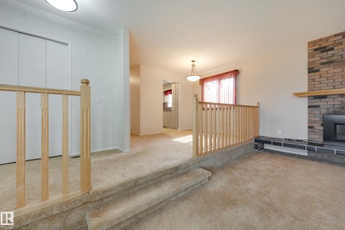 Carpeted steps with wood handrail, brick fireplace with black hearth, built-in shelving, and recessed lighting - 3421 135A Avenue Nw, Edmonton, AB 