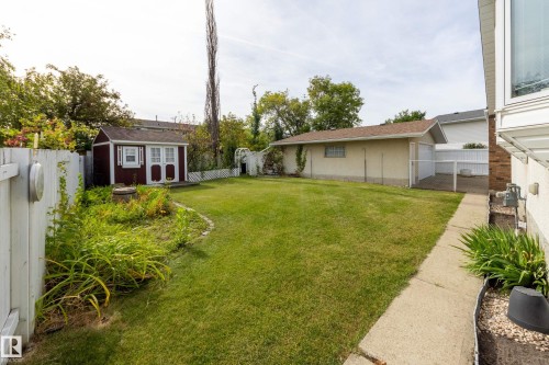 Expansive backyard featuring a manicured lawn, a detached storage shed, a white picket fence, and a concrete pathway - 3421 135A Avenue Nw, Edmonton, AB 