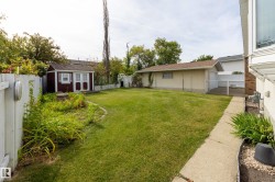 Expansive backyard featuring a manicured lawn, a detached storage shed, a white picket fence, and a concrete pathway - 