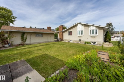 Expansive green lawn with established landscaping, featuring a stucco exterior and bay windows with white louvered shutters - 3421 135A Avenue Nw, Edmonton, AB 