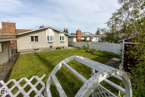 Expansive grassy yard with a white lattice fence and mature trees - 3421 135A Avenue Nw, Edmonton, AB 
