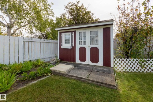 Detached storage shed featuring a red and white exterior, double doors with windowpanes, and a side window with decorative shutters - 3421 135A Avenue Nw, Edmonton, AB 