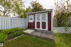 Detached storage shed featuring a red and white exterior, double doors with windowpanes, and a side window with decorative shutters - 