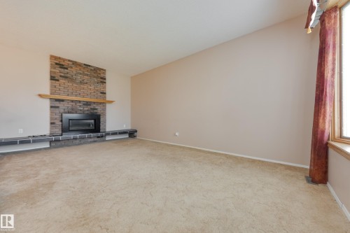 Brick fireplace with a wood mantle, integrated hearth seating, and a large window - 3421 135A Avenue Nw, Edmonton, AB 