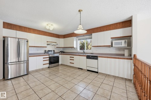 Spacious kitchen featuring tile flooring, white cabinetry with wood-finish accents, stainless steel appliances, and a built-in microwave - 11102 11A Avenue Nw, Edmonton, AB 