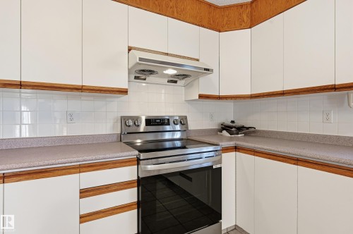 White cabinetry with wood trim, stainless steel range, white tile backsplash, and light-toned countertops - 11102 11A Avenue Nw, Edmonton, AB 