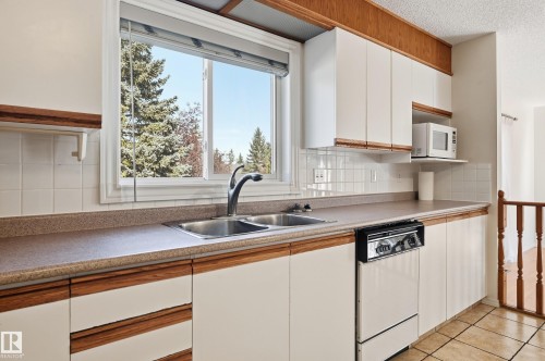 Kitchen with wood-finish trim cabinetry, tiled backsplash, and dual basin sink - 11102 11A Avenue Nw, Edmonton, AB 