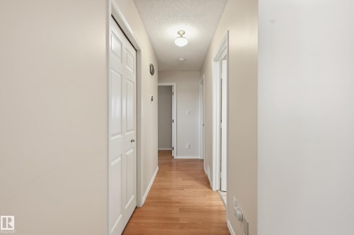 Wood-finish flooring throughout the hallway, featuring light-toned walls and multiple paneled doors - 11102 11A Avenue Nw, Edmonton, AB 