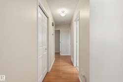Wood-finish flooring throughout the hallway, featuring light-toned walls and multiple paneled doors - 