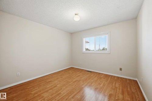 Wood-finish flooring with white baseboards, a white-framed window with blinds, and an overhead flush-mount light fixture - 11102 11A Avenue Nw, Edmonton, AB 