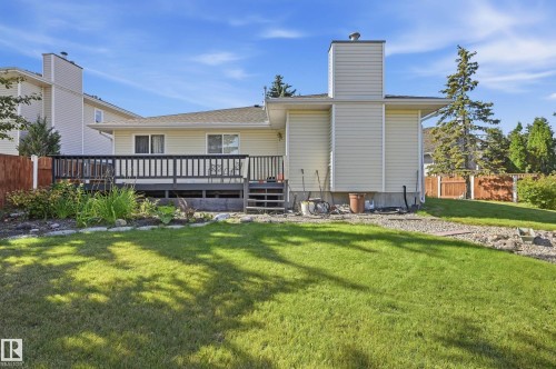 Expansive backyard featuring a manicured lawn, a raised deck with dark railings, exterior siding, and a prominent chimney - 11102 11A Avenue Nw, Edmonton, AB 