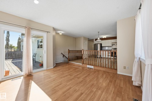 Wood-finish flooring throughout, sliding glass door leading to an outdoor deck, recessed ceiling lighting, and a kitchen with white cabinetry and stainless steel appliances - 11102 11A Avenue Nw, Edmonton, AB 