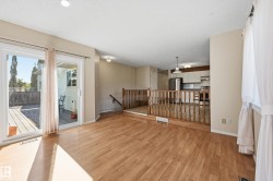 Wood-finish flooring throughout, sliding glass door leading to an outdoor deck, recessed ceiling lighting, and a kitchen with white cabinetry and stainless steel appliances - 