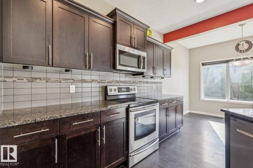 Kitchen featuring dark wood cabinetry, stainless steel appliances, speckled countertops, and a tile backsplash with decorative accent banding - 12007 173 Avenue Nw, Edmonton, AB 