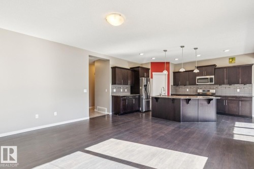 Spacious kitchen featuring dark wood cabinetry, a central island with a sink, stainless steel appliances, and pendant lighting - 12007 173 Avenue Nw, Edmonton, AB 