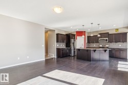 Spacious kitchen featuring dark wood cabinetry, a central island with a sink, stainless steel appliances, and pendant lighting - 
