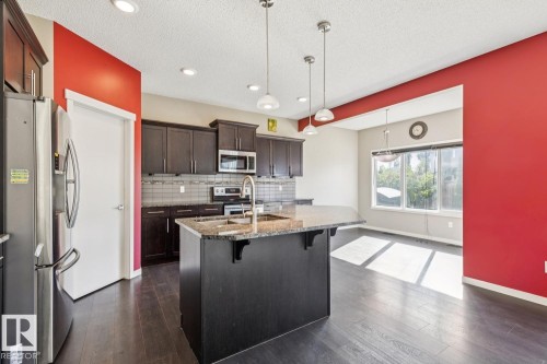 Kitchen featuring a central island with granite-style countertop, stainless steel appliances, dark wood-finish cabinetry, and wood-finish flooring - 12007 173 Avenue Nw, Edmonton, AB 