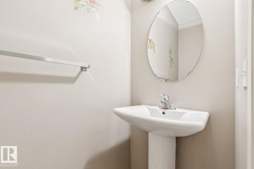 Pedestal sink with a polished chrome faucet, oval mirror, and a wall-mounted towel bar - 12007 173 Avenue Nw, Edmonton, AB 